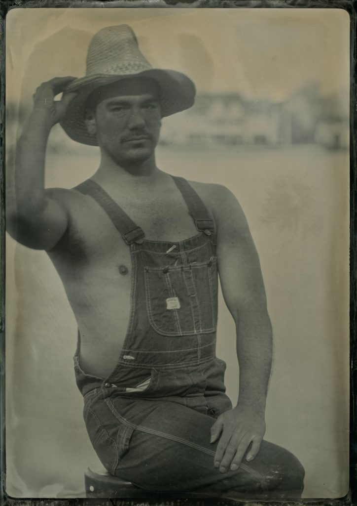 tintype portrait of a male model in straw hat and bibs